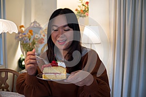Asian Women eating cake at home with happy face expression.