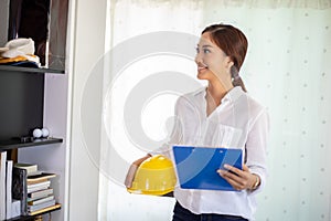 Asian women engineering inspecting and working and holding blueprints at office.she is smiling happy for work