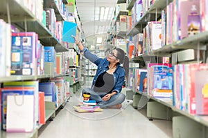 Asian women finding book and reading something in a book,  adult female choosing a book on the bookshelf in a library.