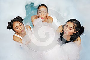 Asian women friends enjoy playing together in foam bobbles pool party
