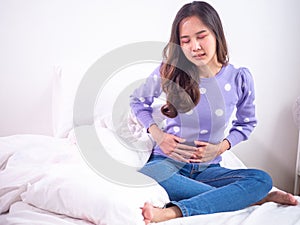 Asian women have stomach ache while sitting in bed in the bedroom after waking up. Menstrual pain concept