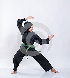 Asian women in hijabs wearing pencak silat uniforms with green belts perform stance movements