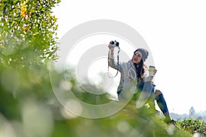 Asian women holding hot tea cup for drinking and take a photo in the morning day, relaxing and sitting outdoor in the tea plantati