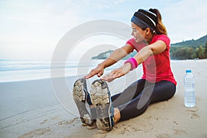 Asian women jogging workout on the beach. Sit down on the beach  fitness relax with stretch legs and Stretch arm