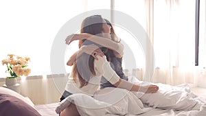 Asian women lesbian happy couple waking up in morning. Asia girls sitting on bed stretching in cozy bedroom at home.