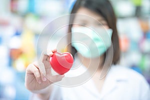 Asian women medical doctor holding a red heart ball with blurred background. Concept of health care