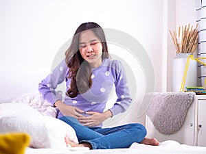 Asian women with menstruation and menstrual cramps. a girl sitting in pain in a bed at home