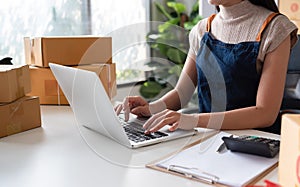 Asian women packing boxes and using a tablet in a home office. Concept of small business and e-commerce