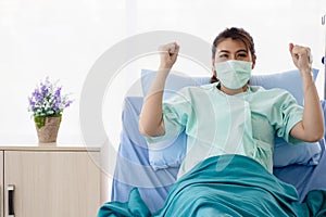 Asian women patient  sitting on hospital bed and raises her arms. The young woman recover from illness. Healthcare and medical