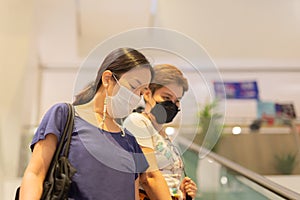 Asian women in protective mask standing on escalator in shopping mall.