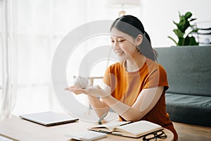 Asian women's hand saving a coin into piggy bank with wooden to calculateon and tablet on the table for business, finance,