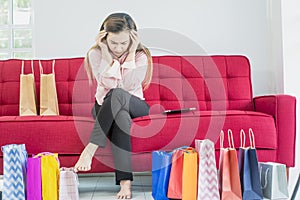 Asian women sit on a red sofa and feel stressed, sad and depressed expression with a lot of colorful shopping paper bags,Concept