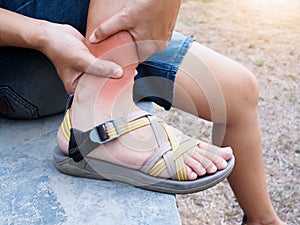 Asian women sitting in park and suffering with leg pain, inflammation of ankle and swelling