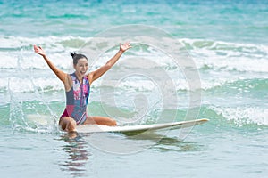 Asian women sitting on a surfboard floating in the sea with small waves, with happy and smile