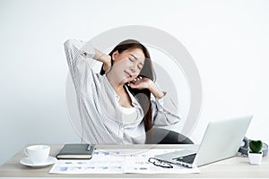 Asian women are tired from work on laptop sits in a chair stretching to relax and unwind while working hard at the office