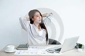 Asian women are tired from work on laptop sits in a chair stretching to relax and unwind while working hard at the office