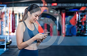 Asian Women are using mobile phones during exercise. She`s standing, typing messages or chatting and smiling happily while stayin