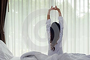 Asian women waking up stretching and raise arms in bed room at home.