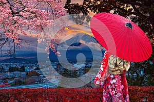 Asian women wear Japanese kimonos. Holding a red umbrella at Mount Fuji and cherry blossoms in Japan