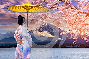 Asian women wear Japanese kimonos. Holding a yellow umbrella at Mount Fuji and cherry blossoms at Lake Kawaguchiko in Japan