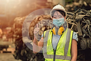 Asian women worker thumbs up waring face mask happy working safety work in a heavy industrial factory with engine machine