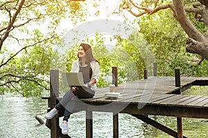 Asian women working and drinking coffee after education nature and forest input the laptop under big tree. The mangrove forest n