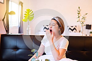 Asian women yawning covering open mouth with hand sitting on sofa, Tired sleepy,Female with symptoms sleepiness photo