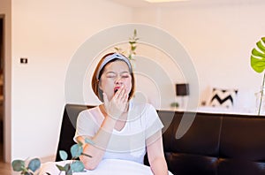 Asian woman yawning covering open mouth with hand sitting on sofa, Tired sleepy,Female with symptoms sleepiness photo