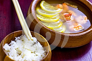 Asian wooden bowl with traditional light spicy thai cuisine rice and tom yam soup with shrimps, seafood and lemon on board