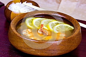 Asian wooden bowl with traditional light spicy thai cuisine rice and tom yam soup with shrimps, seafood and lemon on board