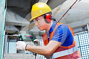 Asian worker drilling in construction site wall