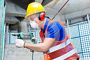 Asian worker drilling in construction site wall