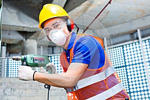 Asian worker drilling in construction site wall
