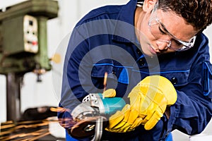 Asian worker grinding metal in manufacturing plant