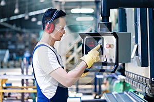 Asian worker operating CNC metal skip in factory