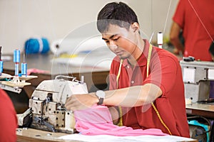Asian worker in textile factory sewing using industrial sewing m