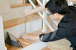 Asian worker using tape measure on ladder
