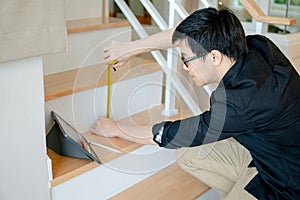 Asian worker using tape measure on ladder