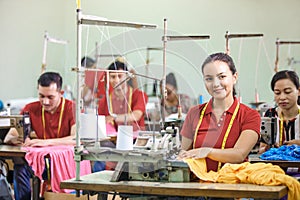 Asian workers in garment factory sewing with industrial sewing m