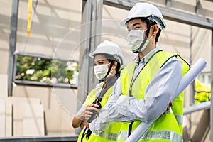 Asian workers people wearing protective face mask onsite of architecture due to covid pandemic crisis. Male and female engineers h
