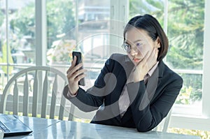 Asian working woman sitting and looking at smartphone Showing a serious expression, wondering, thinking feeling not good