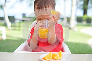 Asian 1 year old toddler baby boy child sitting in high chair holding & drinking tasty orange juice