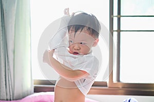 Asian 2 - 3 years old toddler boy child in bed concentrate on putting on his shirt, Encourage Self-Help Skills in Children photo
