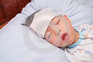 Asian 3 - 4 years old toddler boy child gets high fever lying on bed with cold compress, wet washcloth on forehead to relieve pain photo