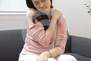 Asian young attractive woman have back pain from work,  rubbing shoulder sitting on sofa at home.