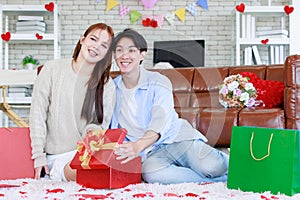 Asian young beautiful female girlfriend sitting smiling opening unboxing red present gift wrapped box on cozy sofa from handsome