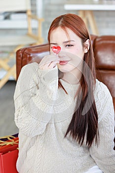Asian young beautiful female shopaholic housewife shopper sitting on fluffy carpet floor with red heart shape paper cutting card