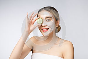 Asian young beautiful smiling woman with flawless complexion holding cucumber slices over eye.