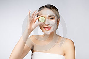 Asian young beautiful smiling woman with flawless complexion holding cucumber slices over eye.
