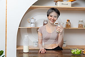 Asian young beautiful woman drinking glass of milk in kitchen at home. health care concept